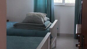 A bedroom with two beds, a window with curtains, a radiator, and a framed picture on the wall.