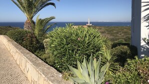 A coastal view with a lighthouse, lush greenery, and a stone wall.