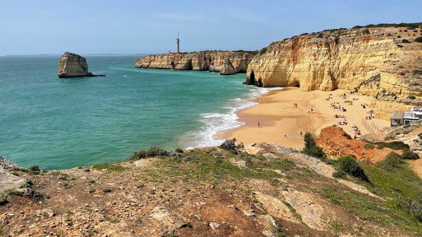 A coastal landscape with a lighthouse, sandy beach, and rocky cliffs.