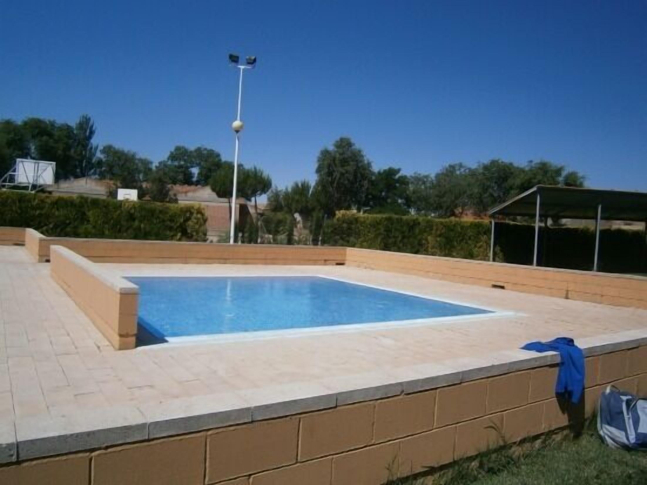 Una piscina rectangular con solárium alicatado, rodeada por un muro de ladrillo y una zona ajardinada.