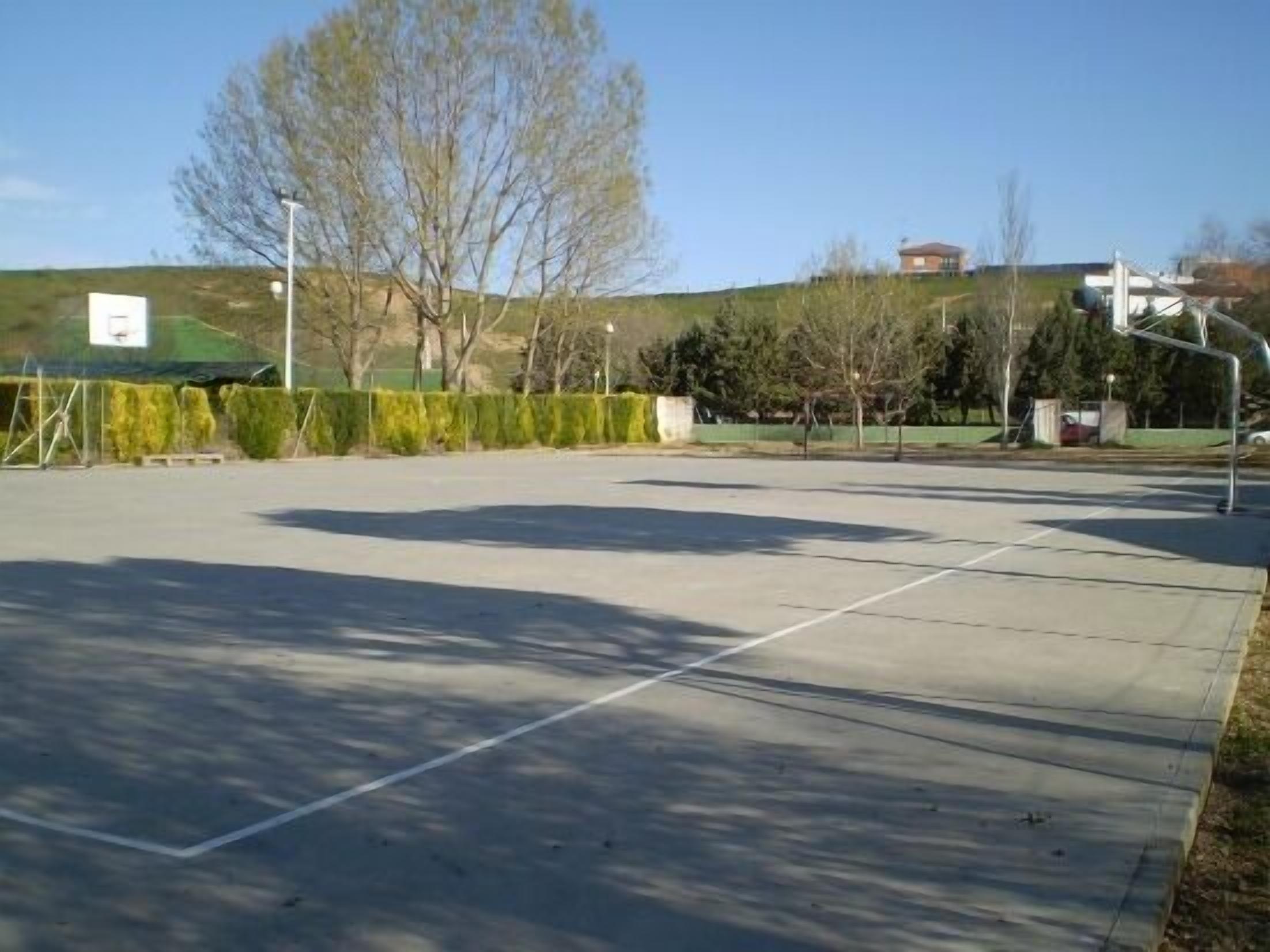 An outdoor basketball court with a clear sky, a green fence, and trees in the background.