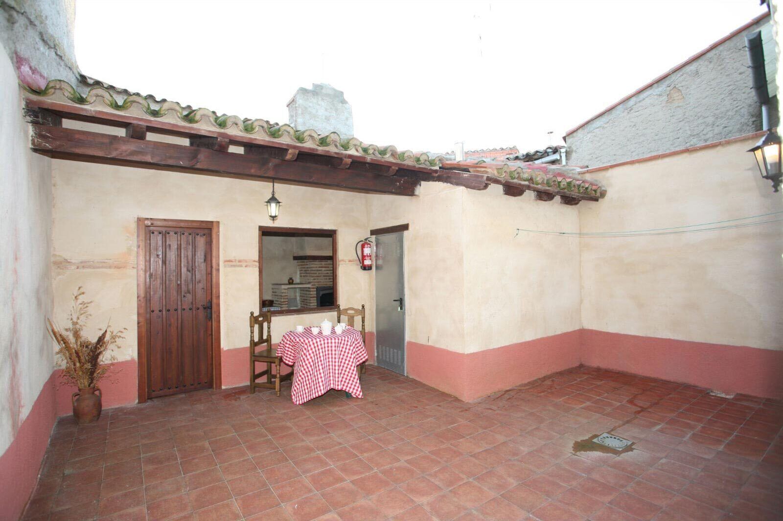 A courtyard with a tiled floor, a wooden door, a table with a checkered tablecloth, and a potted plant.
