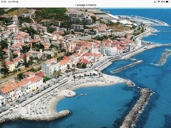 A coastal town with a curved bay, buildings with red roofs, and a rocky shoreline.