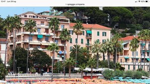 Una playa con filas de tumbonas y sombrillas, un edificio con balcones y palmeras.