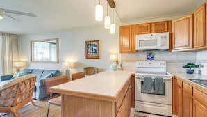 A modern kitchen with wooden cabinets, a central island, a microwave, and a stove. - Gorgeous Oceanfront Condo with Spectacular Views! (Kihei)