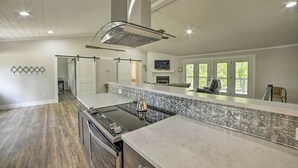 A modern kitchen with a central island, stainless steel appliances, and a large window providing natural light. - Lake Barkley Waterfront Home w/ Deck & Boat Dock! (Cadiz)