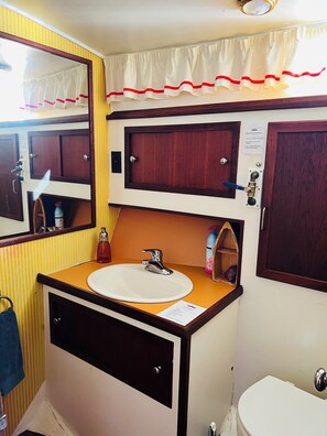 A bathroom with a sink, mirror, cabinets, and a toilet. - Maine Bed & Boat, MAZU on the scenic Damariscotta River (Damariscotta)