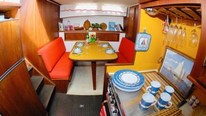 A compact kitchen with a dining area, wooden cabinetry, and a small table set for four. - Maine Bed & Boat, MAZU on the scenic Damariscotta River (Damariscotta)