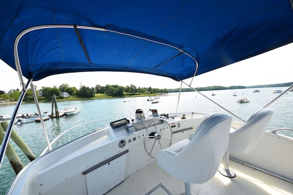 A boat's interior with a steering wheel, control panel, and two white cushioned seats.
