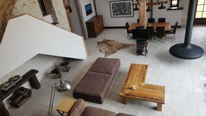 A spacious living area with a high ceiling, wooden beams, a large sofa, a wooden coffee table, and a television. - Restored barn from late 18th century with pool (Champniers)
