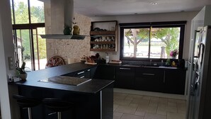 A modern kitchen with a central island, bar stools, a built-in oven, and a large window offering a view of the outdoors. - Restored barn from late 18th century with pool (Champniers)
