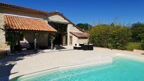 A poolside area with a stone house, outdoor seating, and a clear blue pool. - Restored barn from late 18th century with pool (Champniers)