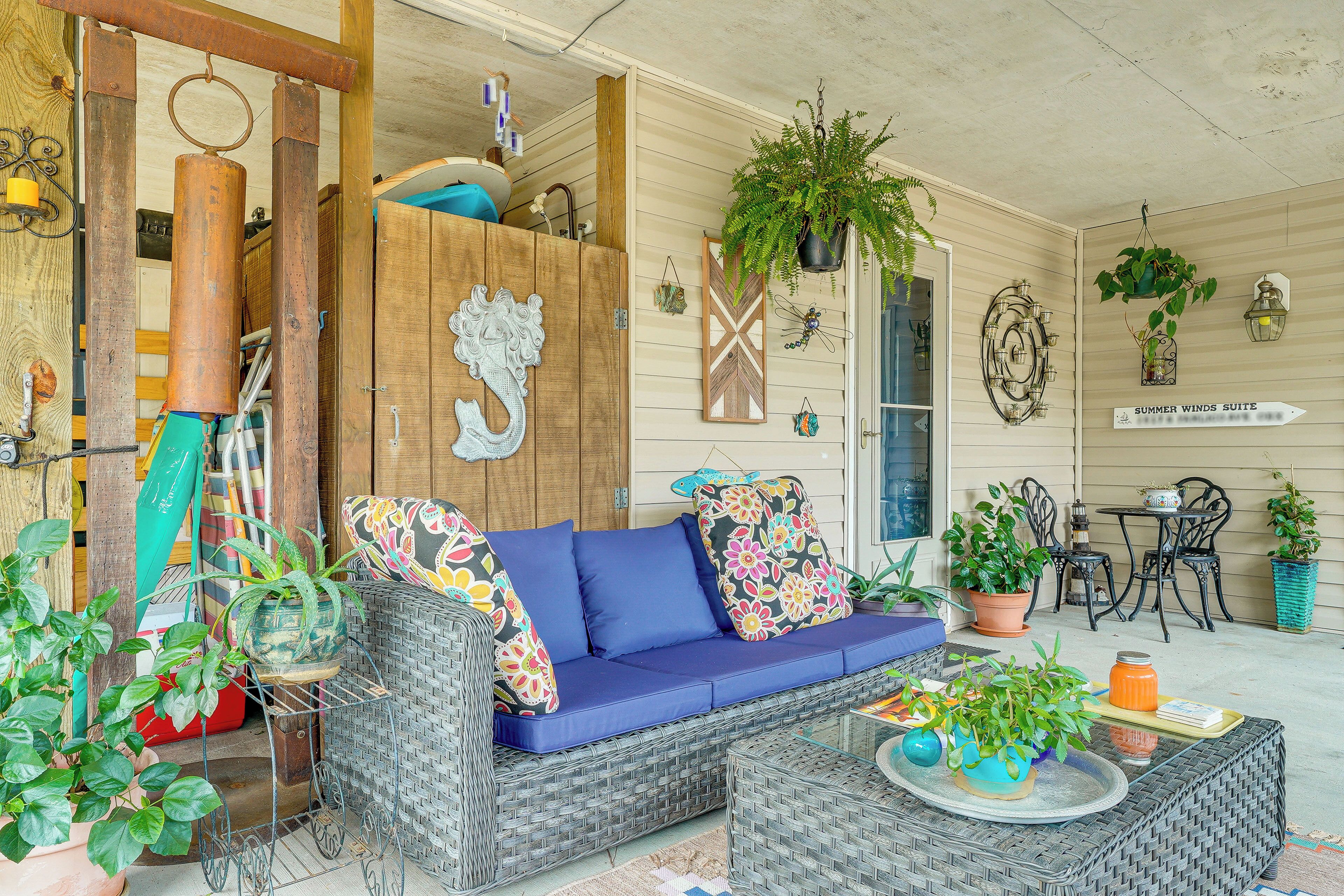 A covered porch with wicker furniture, potted plants, and decorative wall art.