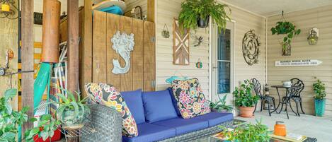 A covered porch with wicker furniture, potted plants, and decorative wall art.