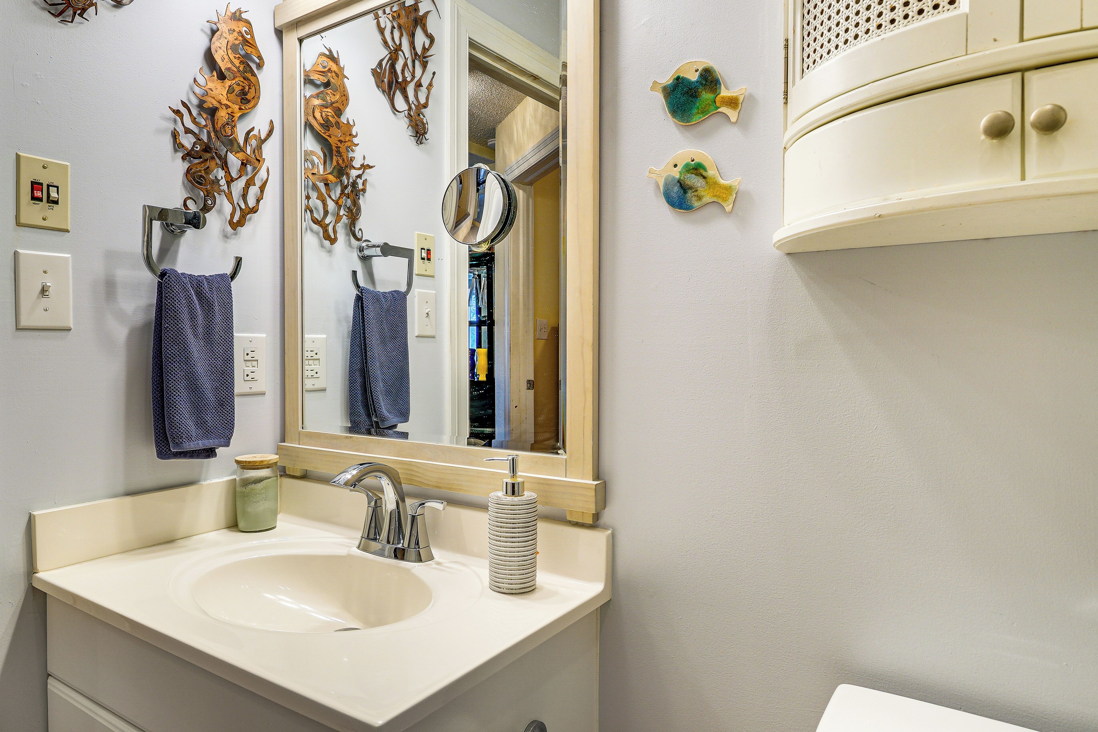 A bathroom with a sink, mirror, and decorative wall pieces.