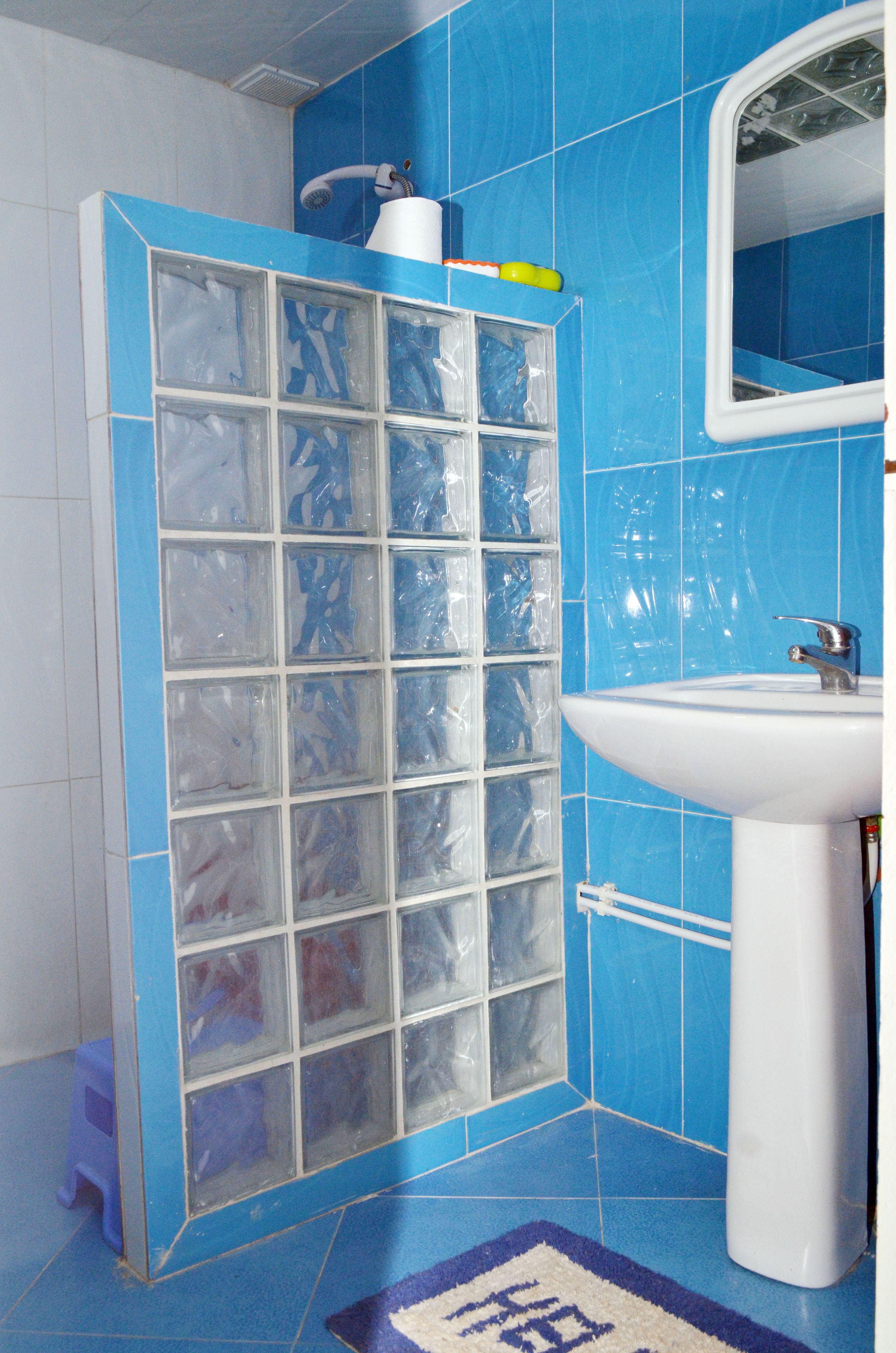 A bathroom with a blue tiled wall, a white sink, and a glass shower enclosure.