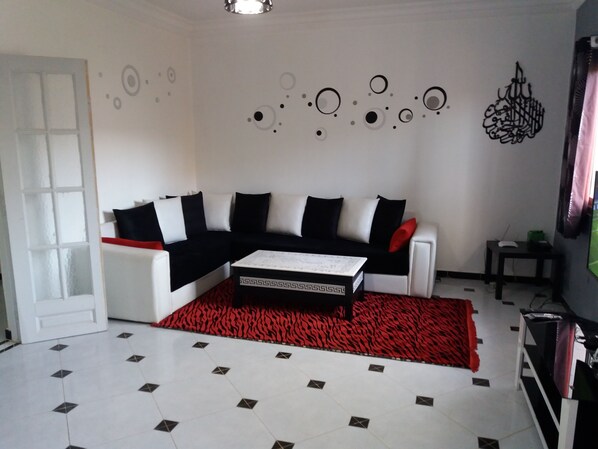 A living room with a white sofa, a patterned rug, and a coffee table. - Chic T3 Akid Lotfi WIFI (Bir El Djir)