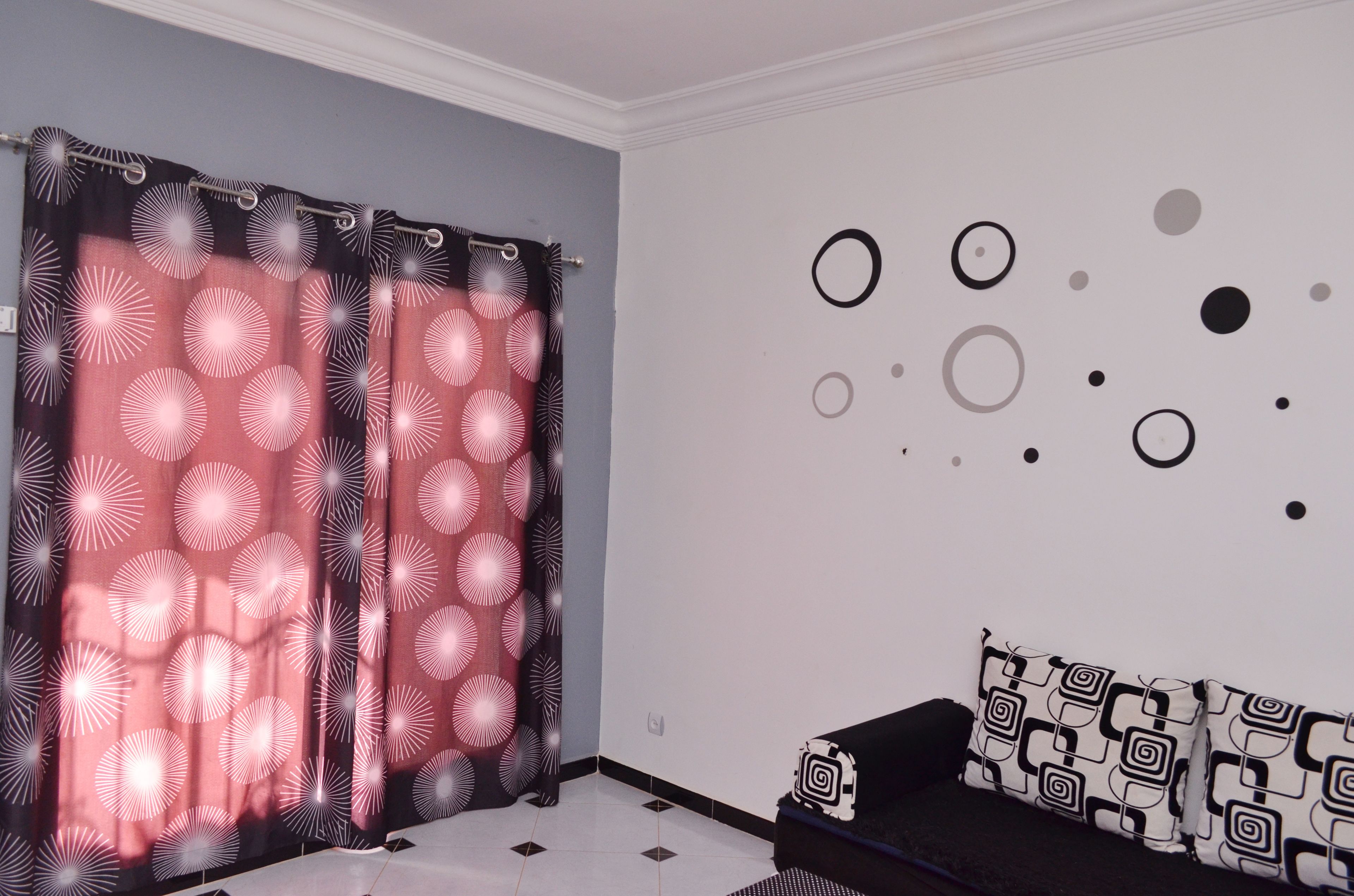 A room with a patterned curtain, a wall with circular decorations, and a black sofa with patterned cushions.