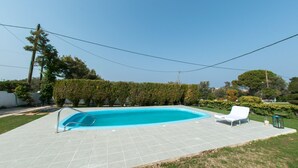 Una piscina rectangular con solárium empedrado, rodeada de setos y árboles.