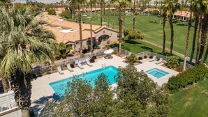Um resort com piscina, palmeiras e um campo de golfe ao fundo.