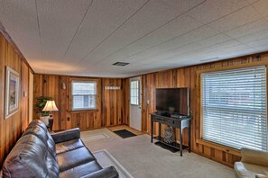A living room with wooden paneling, a leather sofa, a television, and a window with blinds. - Home w/ Lake-View Deck by Camp Perry & Magee Marsh (Port Clinton)
