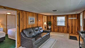 Una habitación con sofá de cuero, cama, paredes de madera, un cuadro enmarcado, lámpara y ventana con persianas.