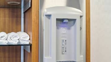 Ein an der Wand montierter Wasserspender mit Sensor, eine Glasablage mit gerollten Handtüchern und eine Holzvertäfelung.