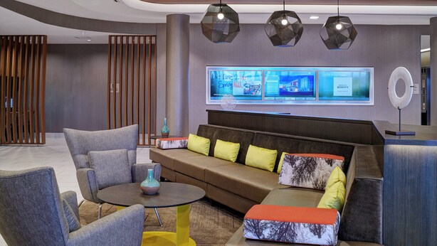 Eine moderne Lobby mit Ecksofa, Sessel, Couchtisch und einer Wanddeko mit digitalen Anzeigen.