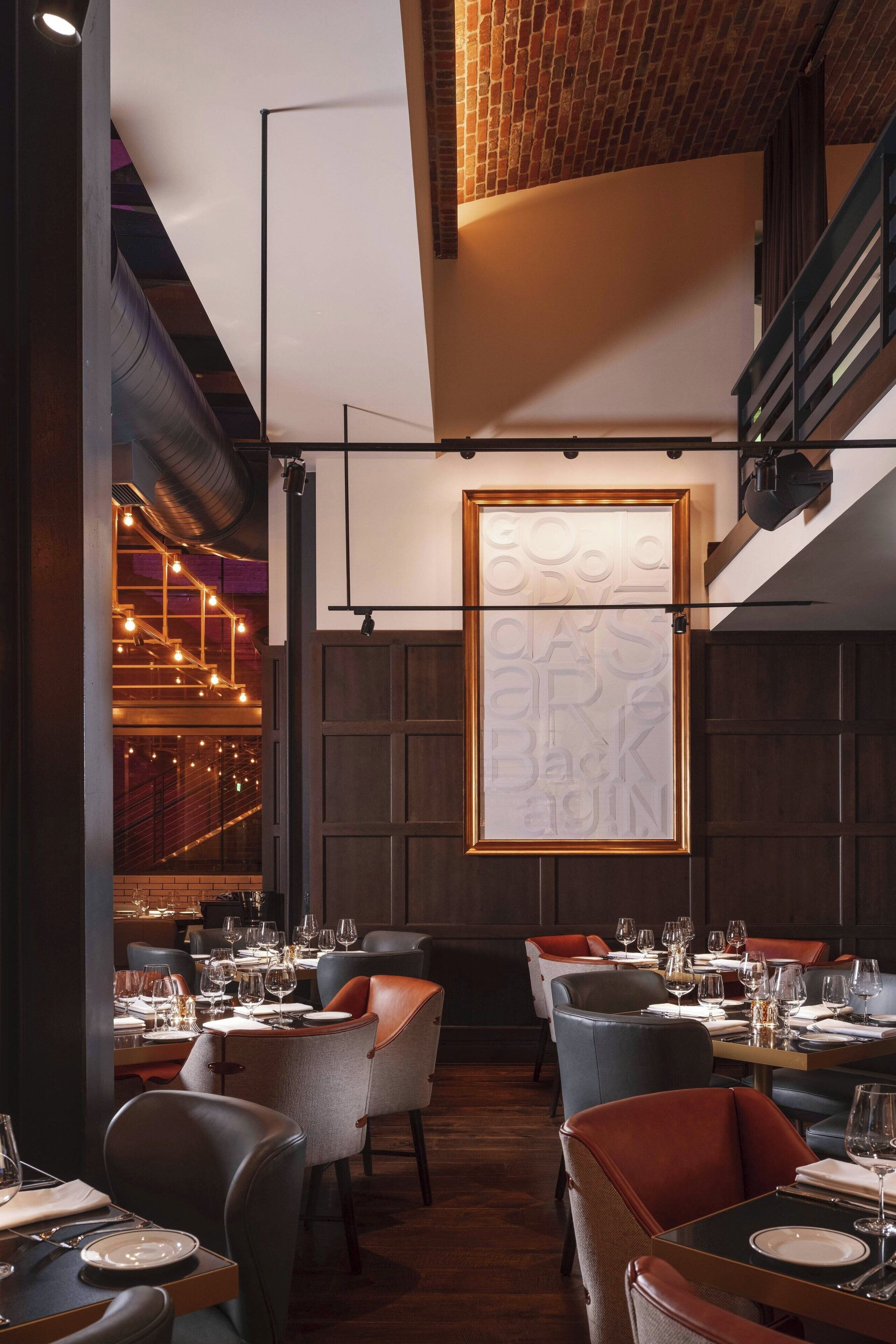 Interior de restaurante con paneles de madera, un ventanal con diseño en vidrio esmerilado y mesas dispuestas para comer.