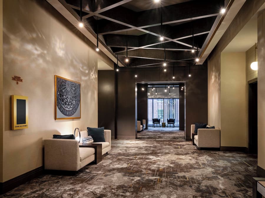 Un hall d’hôtel moderne, doté d’un plafond haut, d’un éclairage aux formes géométriques et d’un sol recouvert de moquette.