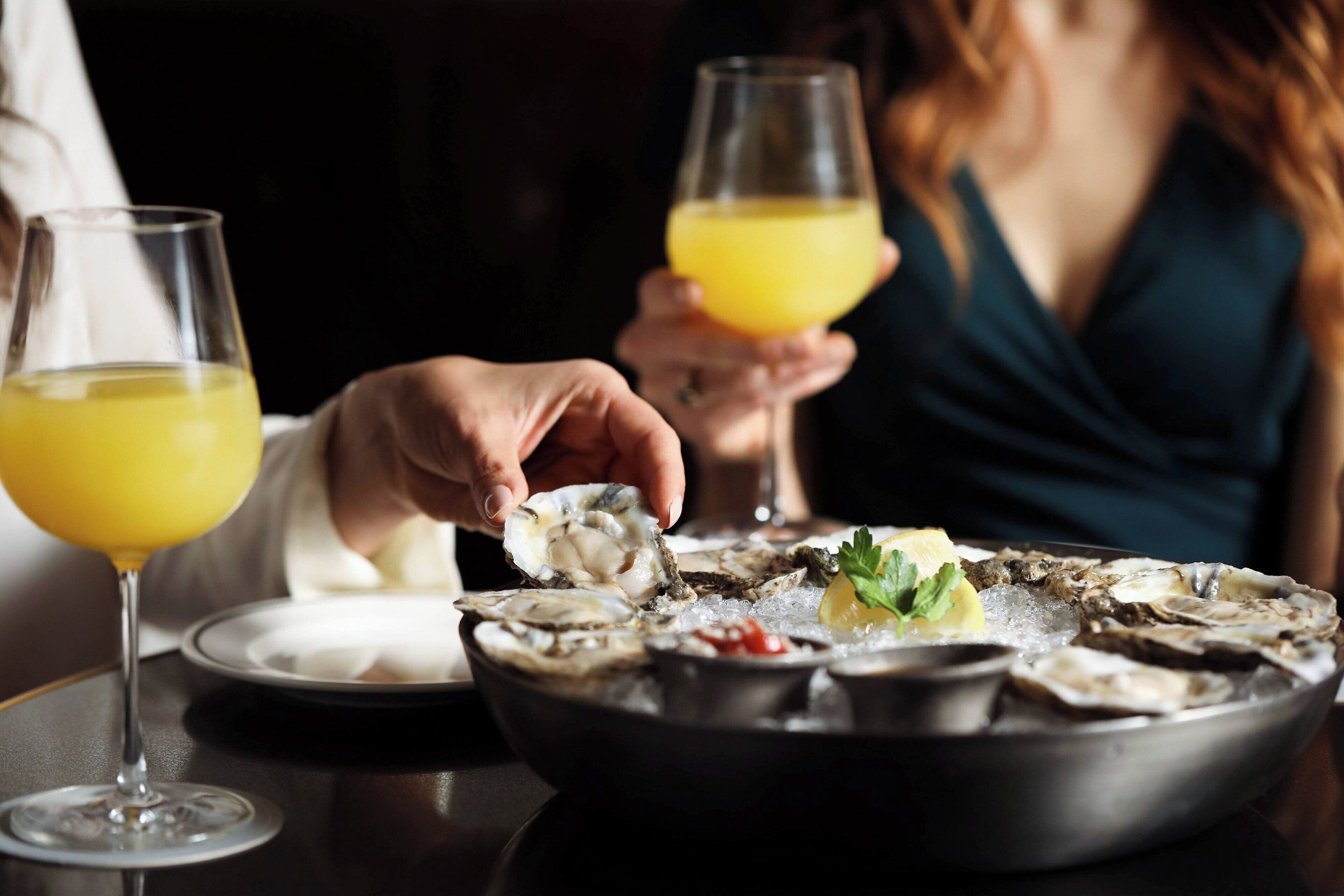 A dining table with a plate of oysters and a glass of orange juice.