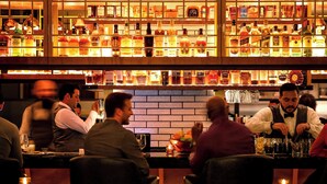 Eine Bar mit Regalen voller Spirituosenflaschen und einem Barkeeper, der Getränke zubereitet.