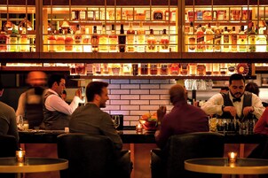 Un bar con estantes llenos de botellas de licores y un cantinero preparando tragos.