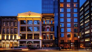 Ein mehrgeschossiges Hotel mit einer klassischen Fassade, großen Fenstern und einem modernen Glasgebäude daneben.
