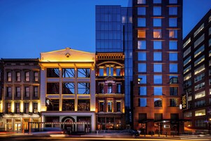 Un hotel de varios pisos con fachada clásica, ventanas amplias y un edificio moderno de vidrio adyacente.