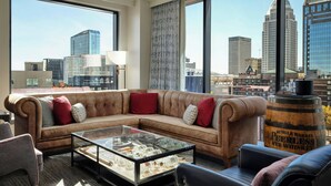 Ein modernes Wohnzimmer mit einem ledernen Ecksofa, einem Glastisch und Blick auf die Skyline der Stadt durch große Fenster.