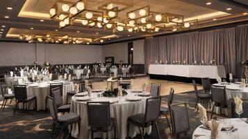 A large banquet hall with round tables set for dining, featuring chandeliers and a stage area.