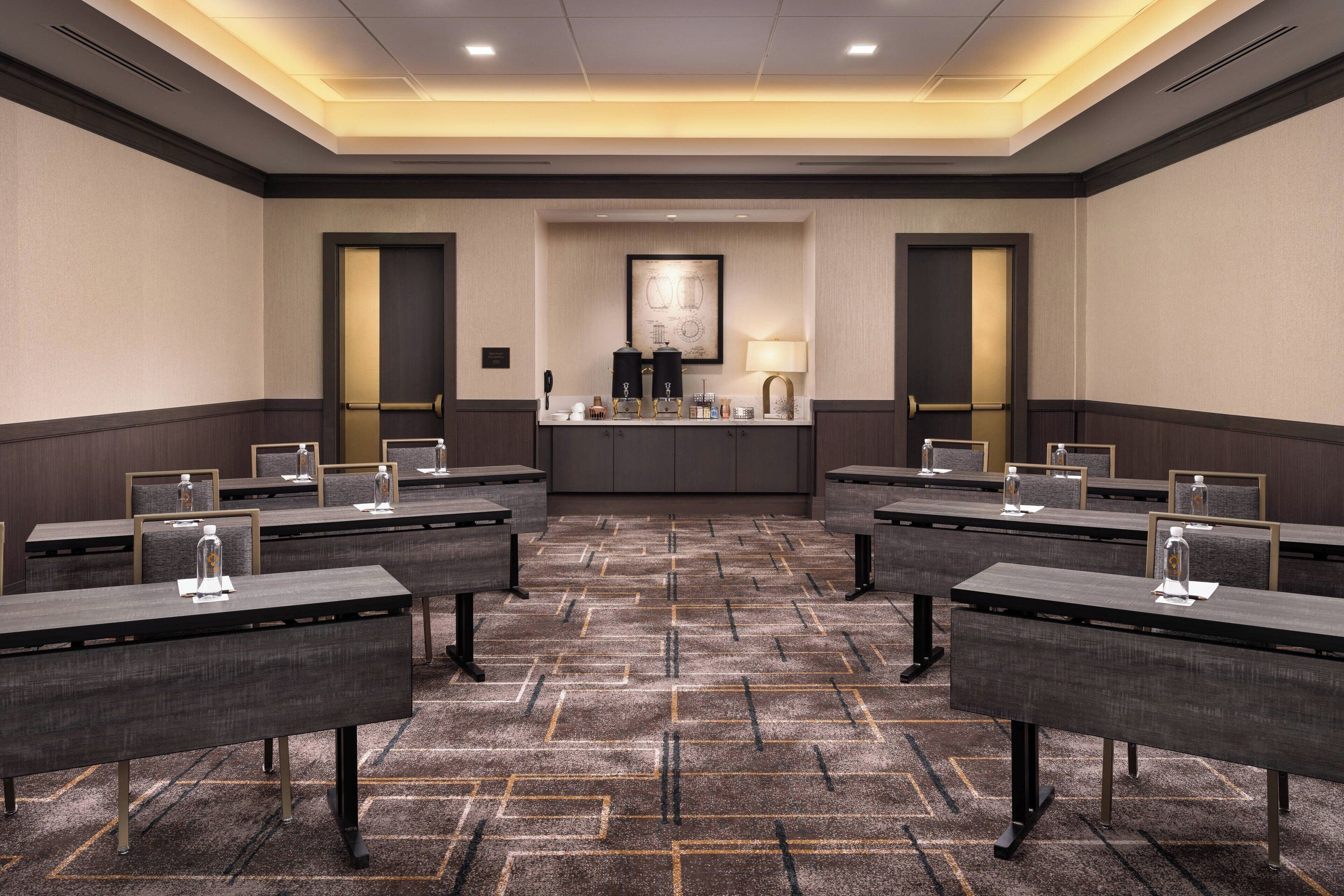 A conference room with multiple tables, a central counter with a coffee machine, and a framed picture on the wall.