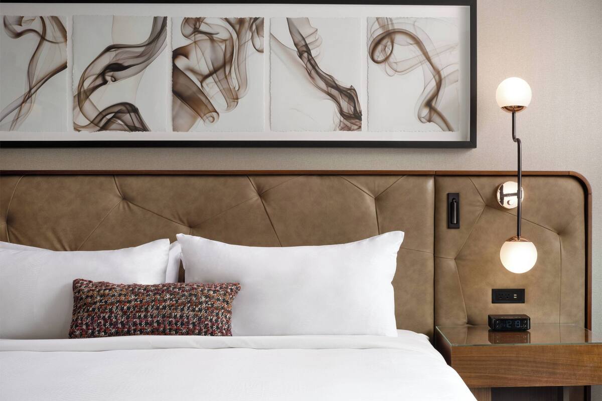A neatly made bed with white and patterned pillows, a tufted headboard, and a bedside table with a lamp and clock.