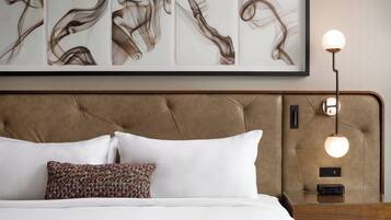 A neatly made bed with white and patterned pillows, a tufted headboard, and a bedside table with a lamp and clock.