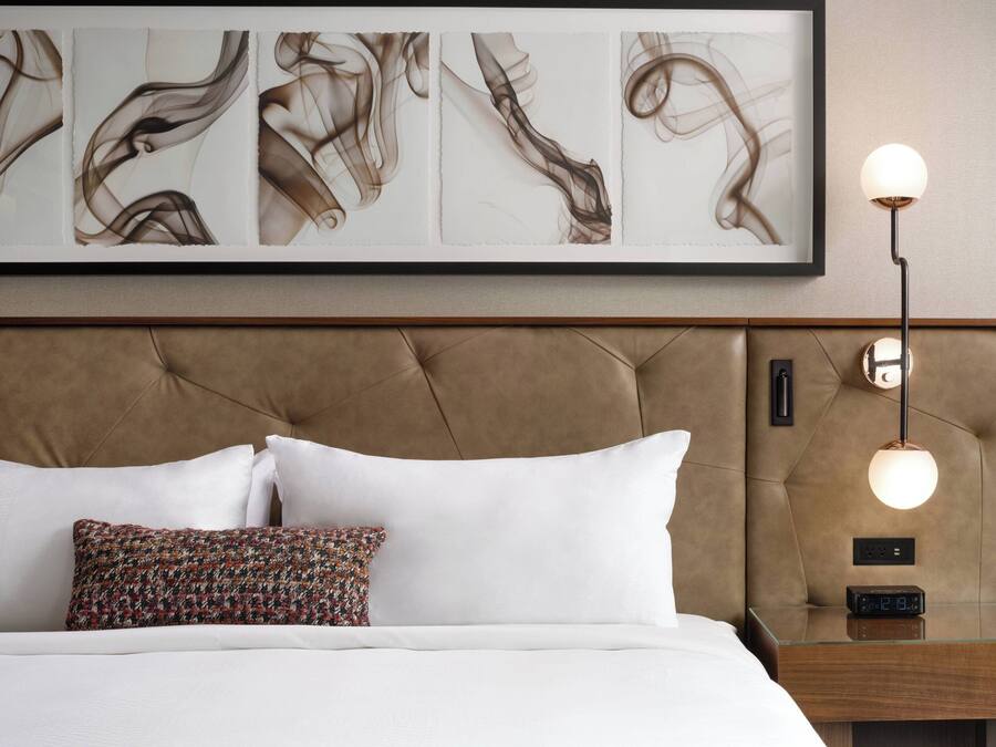 A neatly made bed with white and patterned pillows, a tufted headboard, and a bedside table with a lamp and clock.
