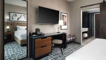 A hotel room with a bed, a desk with a chair, a TV mounted on the wall, and a large mirror.
