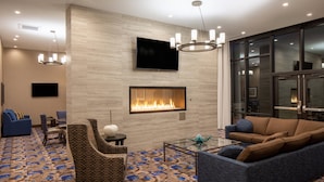 A modern hotel lobby with a fireplace, comfortable seating, a flat-screen TV, and a large window offering a view. - Residence Inn by Marriott Seattle South/Renton (Renton)