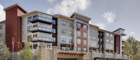 A multi-story hotel with a modern design, featuring balconies, a covered entrance, and a landscaped outdoor area.