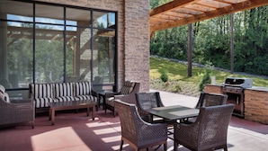 An outdoor patio with wicker furniture, a stone wall, and a view of a forest. - Residence Inn by Marriott Seattle South/Renton (Renton)