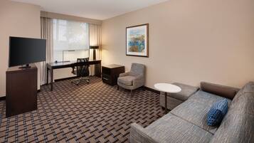 A hotel room with a large flat-screen TV, a desk with a chair, a sofa, and a small round table.