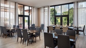 A spacious dining area with multiple tables and chairs, large windows offering views of the outdoors, and a modern interior design. - Residence Inn by Marriott Seattle South/Renton (Renton)