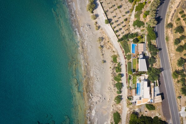 An aerial view of a coastal property with a swimming pool, a road, and sparse vegetation. - Villa Ammos,  great view by the beach, next to the sea  (Ferma)