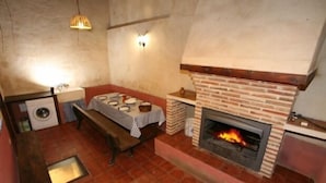 Une cuisine de taille modeste avec une cheminée en briques, une table à manger recouverte d’une nappe à carreaux et un lave-linge.