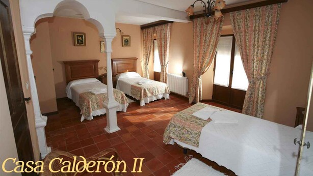 Une chambre d’hôtel avec deux lits, une grande fenêtre avec des rideaux, un radiateur et un lustre.